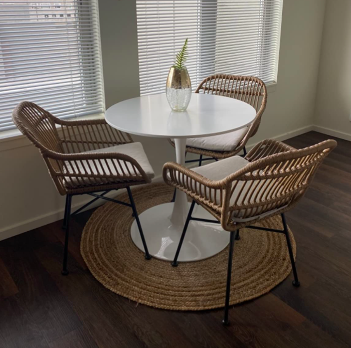 Reviewer’s rattan chairs featuring light tan woven material, a modern square silhouette, and sturdy black metal legs. Positioned around a white tulip table with a woven circular accent.