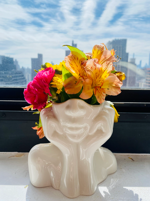 A white vase featuring the lower half of a face, with the figure resting its head in its hands