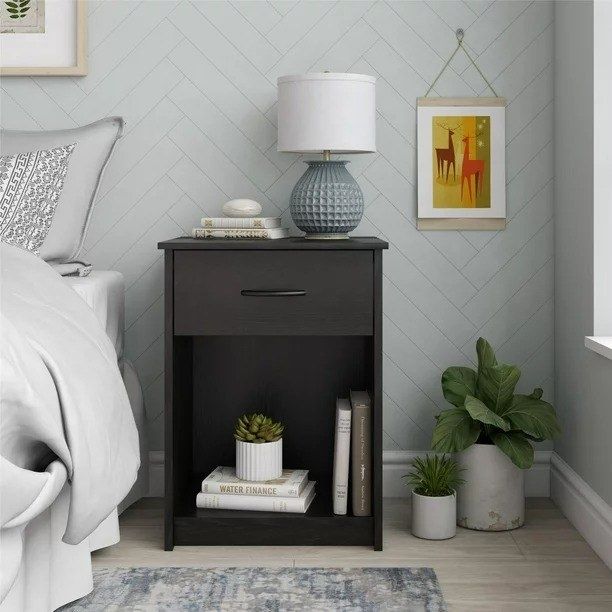 A sleek black oak nightstand in a bedroom with a lamp on top and books neatly stored inside