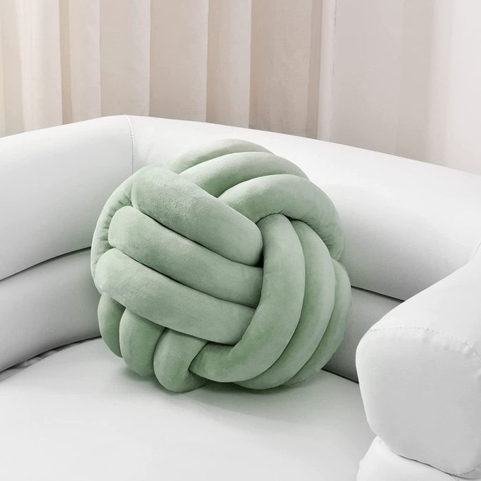 A sage green pillow shaped like an intricate knot