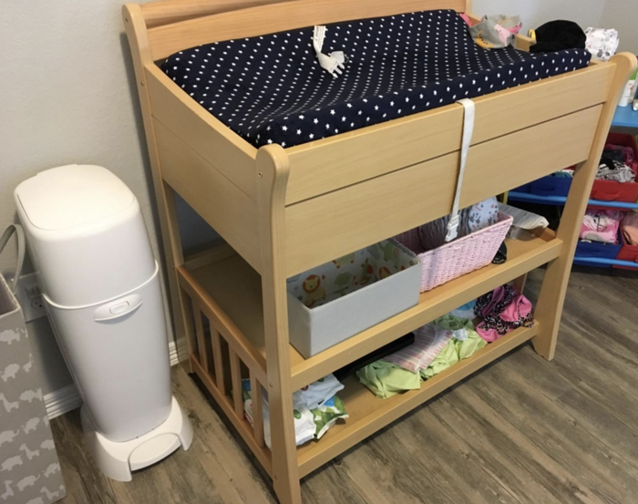 A reviewer’s photo of the Diaper Genie placed next to a changing table