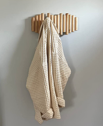 The rack attached to a wall, with one of its cylindrical hooks extended to hold a jacket