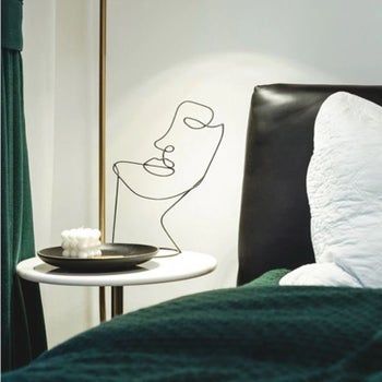 A black wire sculpture resembling an abstract face, displayed on a nightstand.