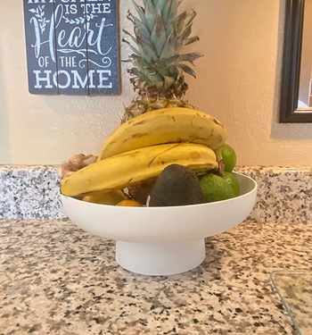 A small white raised fruit bowl filled with bananas and apples