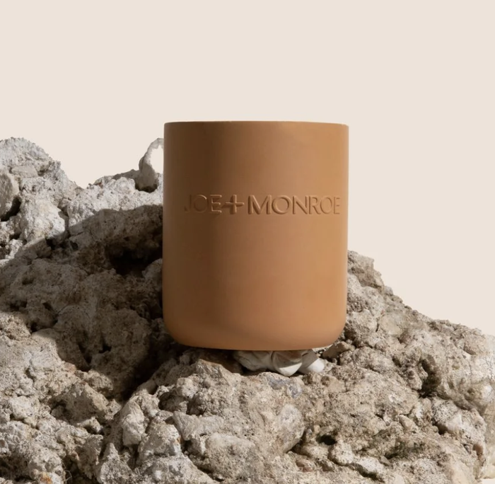 A clay-colored candle sits on a rock.