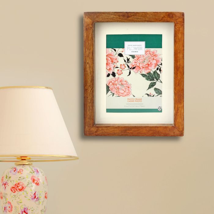 A brown wooden photo frame displayed on a wall next to a lamp
