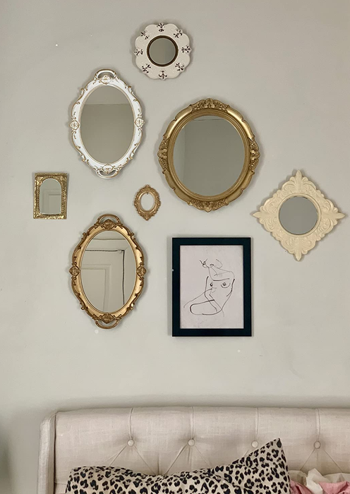 The white and gold variants of the mirror positioned on a wall next to artwork and other mirrors, creating a gallery-style wall