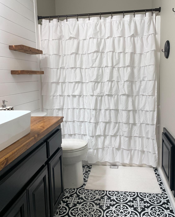 A reviewer's photo of the white ruffled shower curtain hanging in their bathroom.