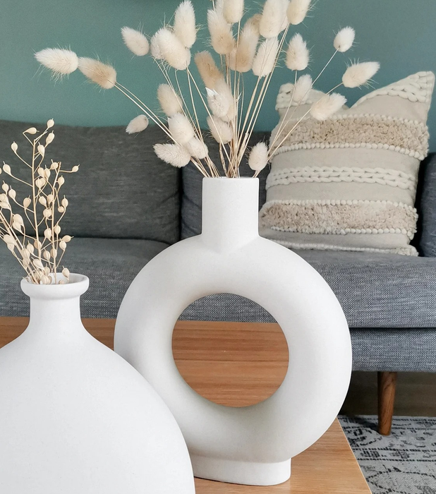 A chic white donut-shaped vase holding dried plant sprigs, positioned beside the hourglass vase for a stylish pairing.