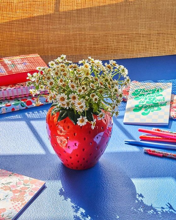 A large strawberry-shaped vase filled with fresh daisies