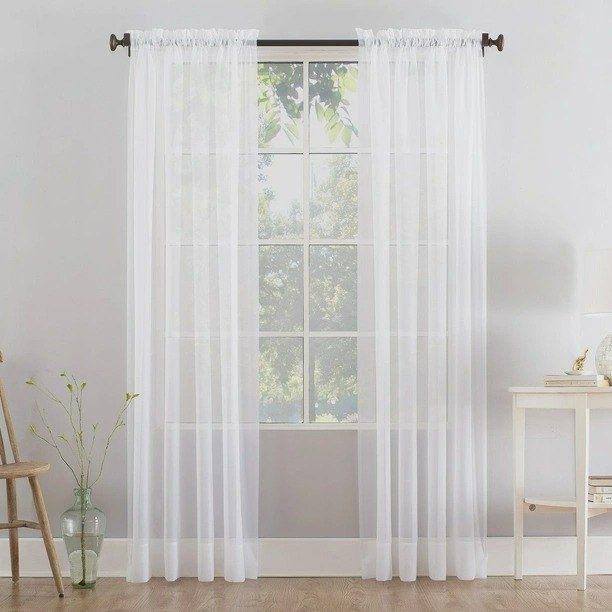 A white curtain panel hanging from a rod near a window in a room