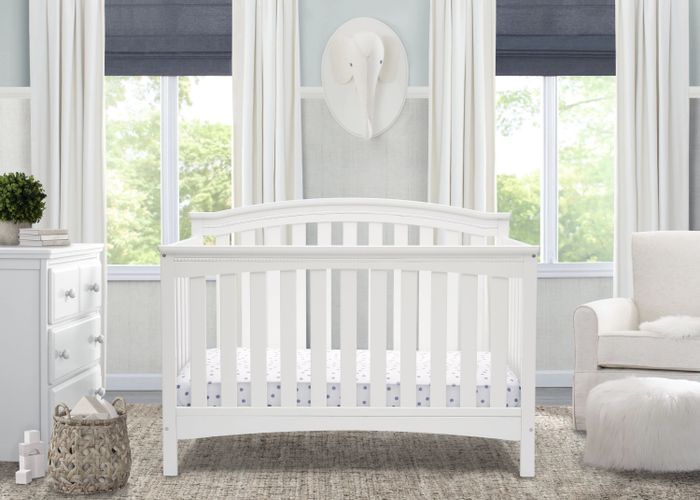 A white convertible crib placed in a nursery, offering multiple functions for growing children.