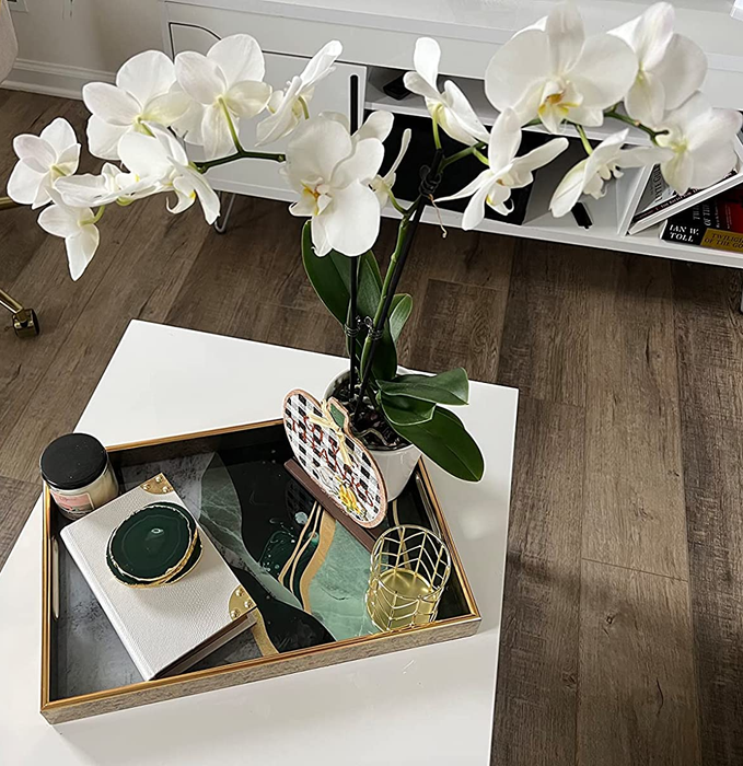 A reviewer’s photo of the green and gold tray, now holding a vase of orchids, on a coffee table.
