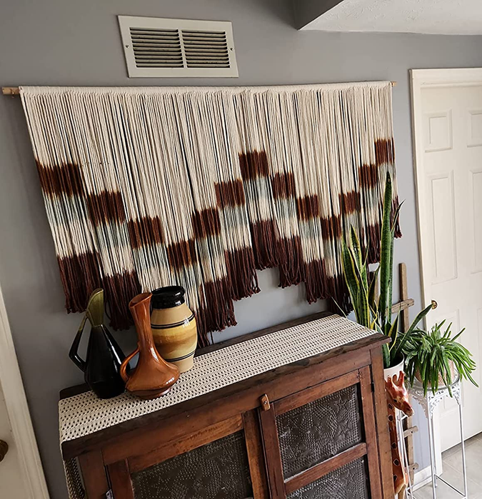 A reviewer’s photo of the brown, gray, and white macrame wall hanging displayed above a cabinet.