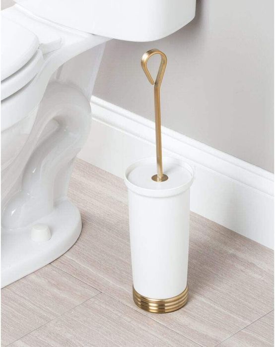 The white and gold toilet brush holder set placed in a bathroom.