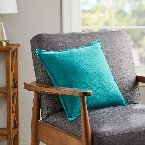A teal decorative pillow resting on an accent chair