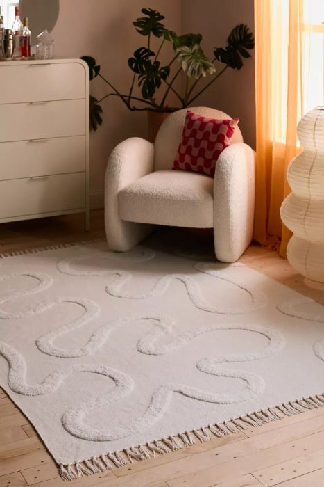 A cozy chair paired with a textured white rug and a dresser in a chic room, ideal for contemporary home decor.