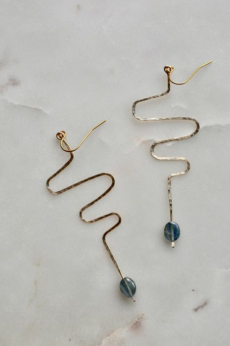 An image showing brass squiggle earrings with blue stones at the bottom