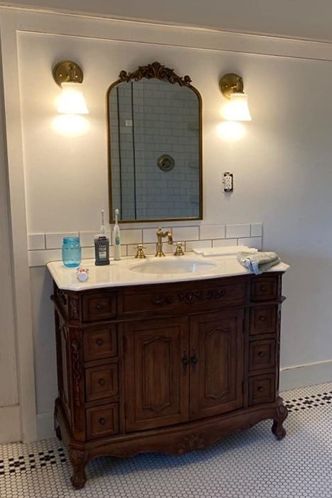 A golden mirror with extra gilding at the top, hanging above a bathroom sink.