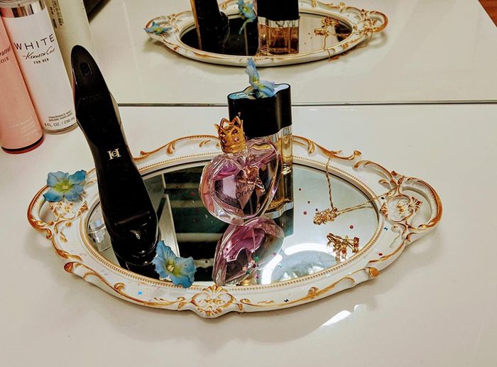 Perfume and other small items displayed on a white and gold mirror being used as a tray