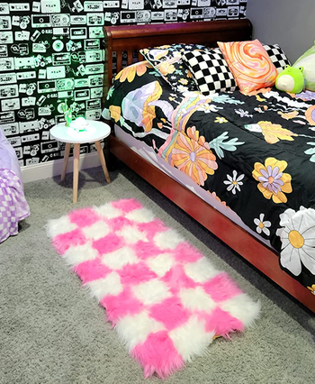 A rectangular pink and white checkerboard rug placed beside a bed