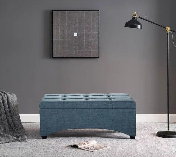 A blue storage ottoman placed on the floor in a bedroom, offering both style and practicality.