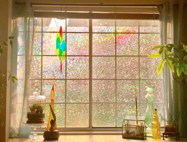 A user's window bathed in light, casting muted colors from a translucent rainbow film that adds a shimmering effect to the glass
