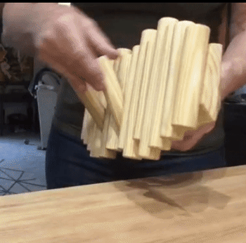 A reviewer showcasing a light wood rack with cylindrical hooks, demonstrating how every other cylinder can be pulled out to create a functional hook