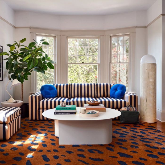 A modern living room features a striped sofa and a round white coffee table, with a bold leopard print rug adding an eye-catching touch. Large windows allow natural light to flood the space, enhancing its open, airy feel.