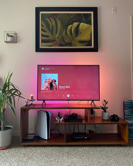 A reviewer's photo of the wooden TV console, backlit with vibrant pink and orange lights, adding an extra touch of flair.
