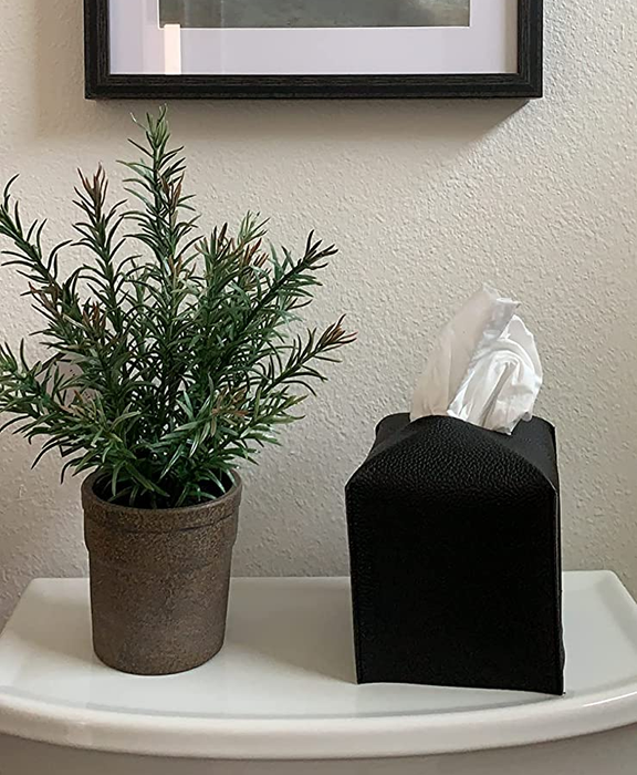A photo of the black tissue box cover placed on a shelf beside a plant.