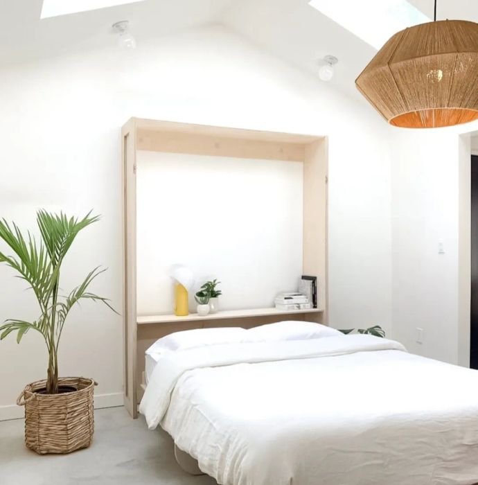 A minimalist bedroom featuring a Murphy bed, wicker lamp, and a potted plant
