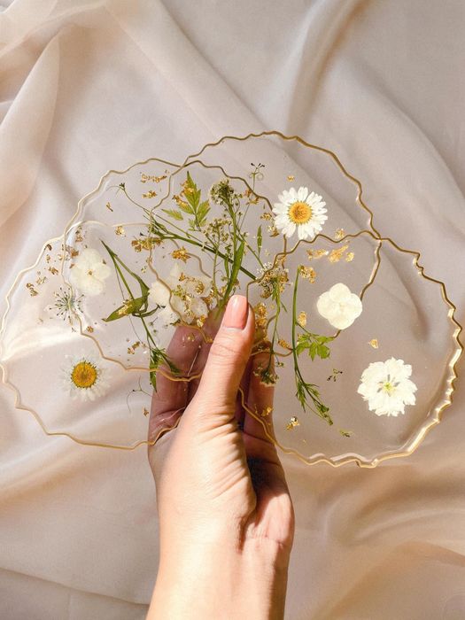 A set of clear coasters featuring delicate white pressed flowers encased within, complete with an elegantly irregular gold rim.