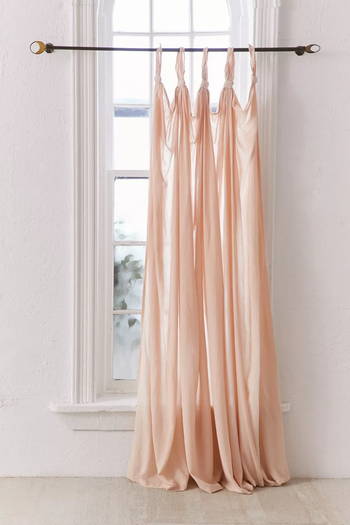 A soft pink sheer curtain, tied with a knot at the top, draped over a window.