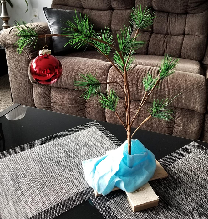 A reviewer photo of the Charlie Brown Christmas tree, adorned with a single red ornament and Linus's blue blanket draped beneath it