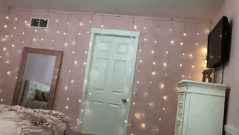 The lights hang vertically, flickering in a mesmerizing pattern against a soft pink bedroom wall.