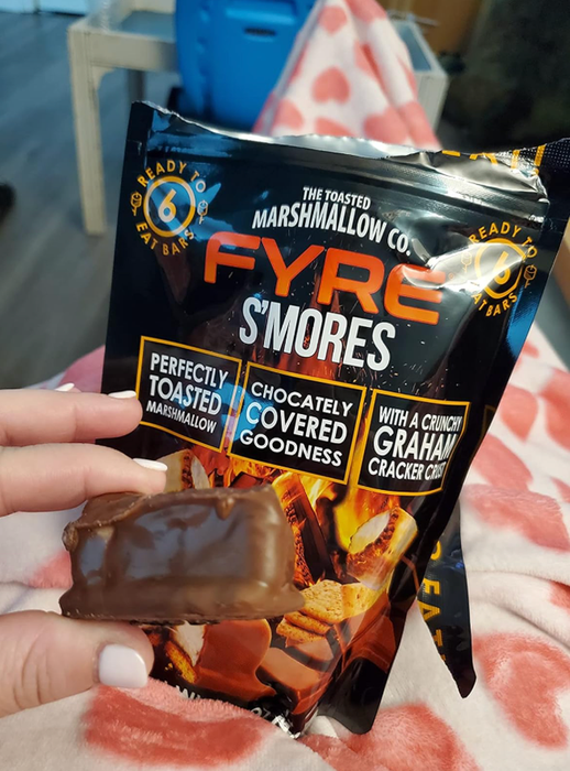 A hand holding a chocolate-dipped s'more with a partially visible package labeled 