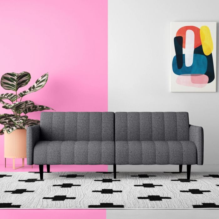 A modern gray sofa against a vibrant background split in pink and white halves