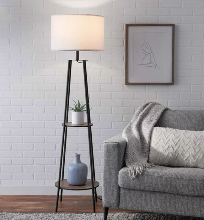 A black standing lamp with a shade and built-in shelves for additional storage or decoration.