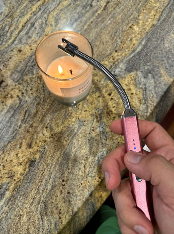A hand ignites a candle with a flexible, rechargeable lighter on a kitchen countertop.