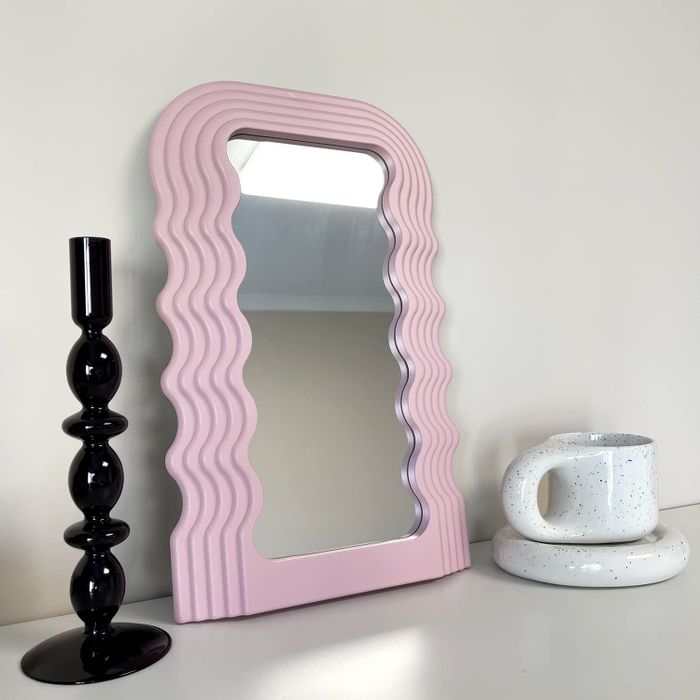 a tabletop featuring a medium-sized mirror with a wavy frame