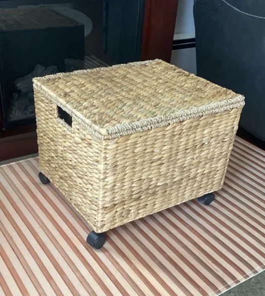 a woven storage basket with a lid and wheels, resting on a striped rug, perfect for home organization
