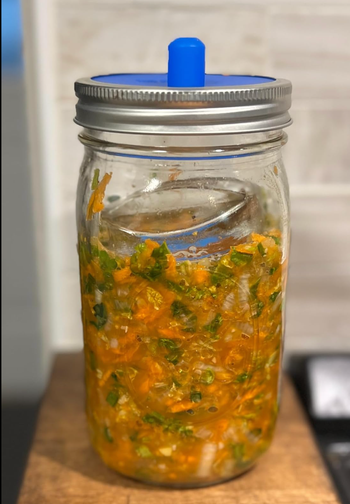 A jar of homemade fermented vegetables with a fermentation lid, sitting on a kitchen counter.