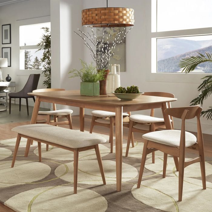 A stylish dining room set featuring a wooden table, matching chairs, a bench, and light upholstery. Decorative plants and a woven light fixture enhance the overall aesthetic of the space.