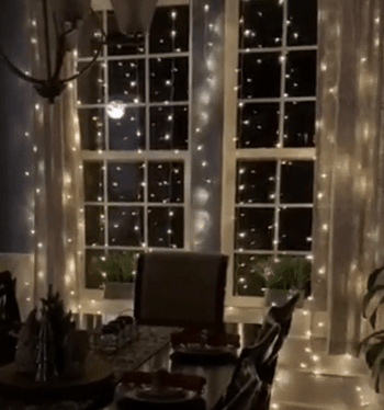 reviewer gif showing twinkling lights hung in front of the windows in their dining room