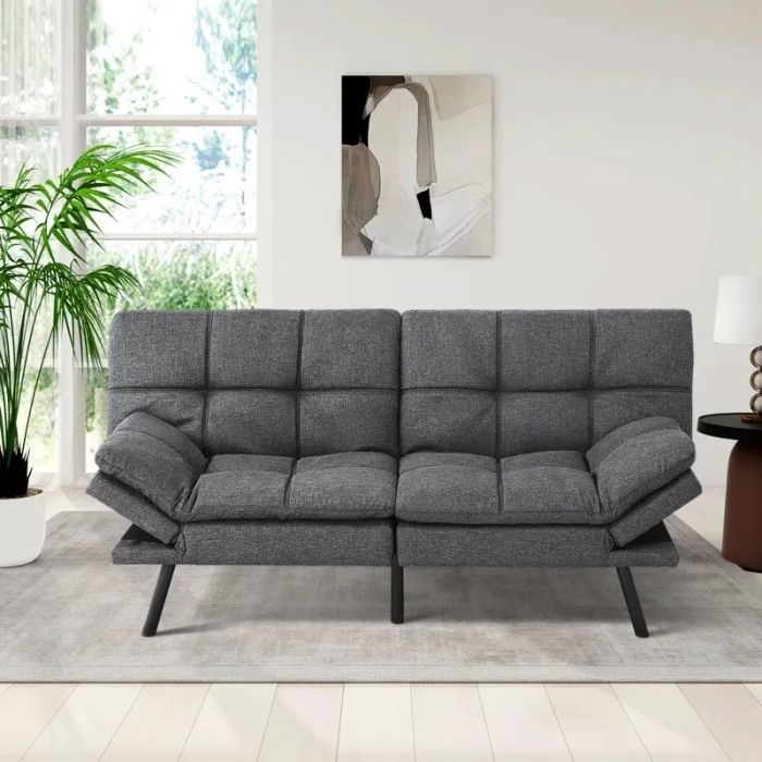 A chic grey futon is set in a modern, minimalist living space, complete with a large plant, abstract art on the walls, and sleek, contemporary decor elements.