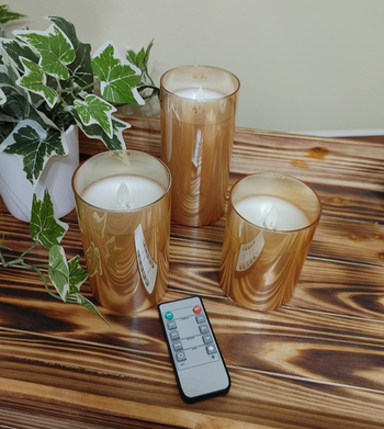 A reviewer's image showcasing three unlit candles of varying sizes, accompanied by a small remote.