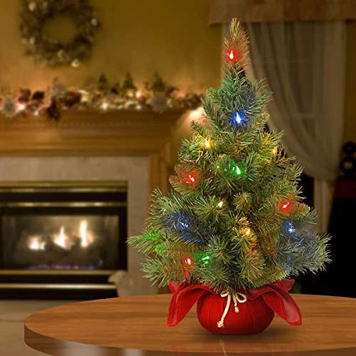 The illuminated mini tree sitting on a table in front of a cozy fireplace