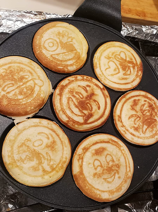 A pan with mini pancakes, each showing a different expression cooked into them