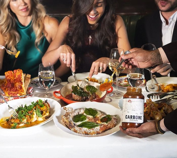 A waiter serving dishes with the sauce as diners enjoy their meals